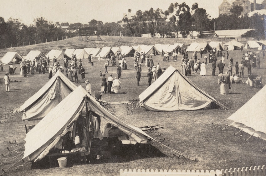 A black and white image of dozens of white tents set up on an oval with people milling about