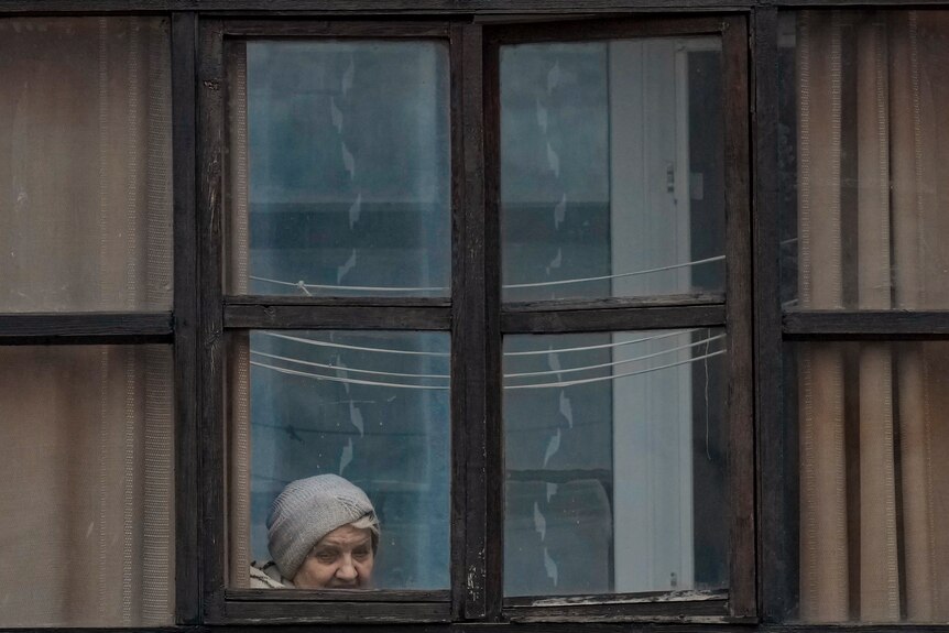 Женщина смотрит в окно балкона в Луганске.