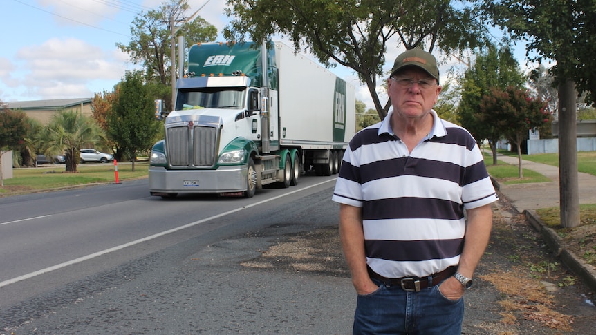 A man in a striped shirt with a truck driving behind him