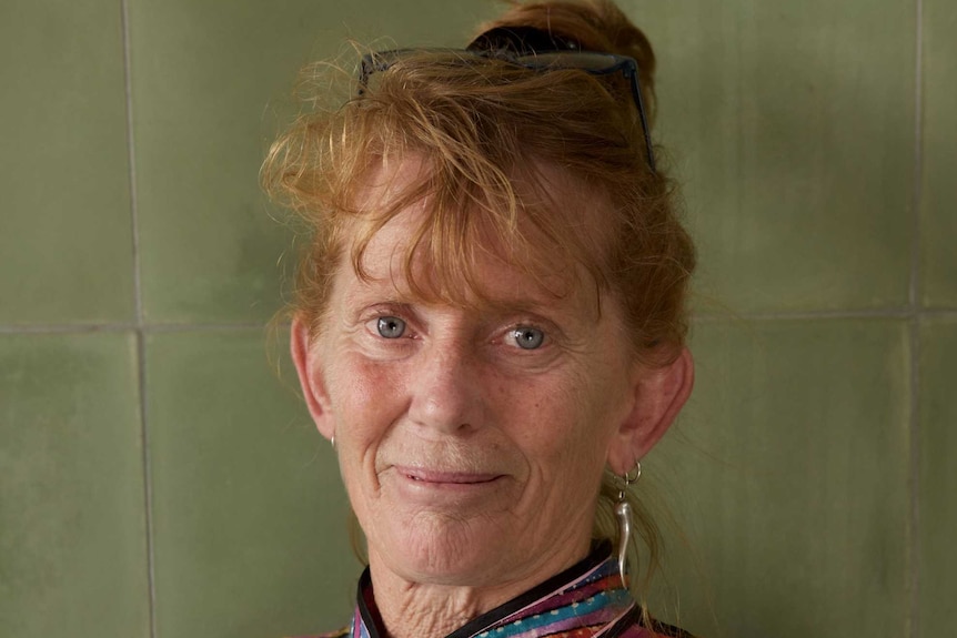 A profile photo of a red haired woman in a colourful dress standing and looking at the camera.