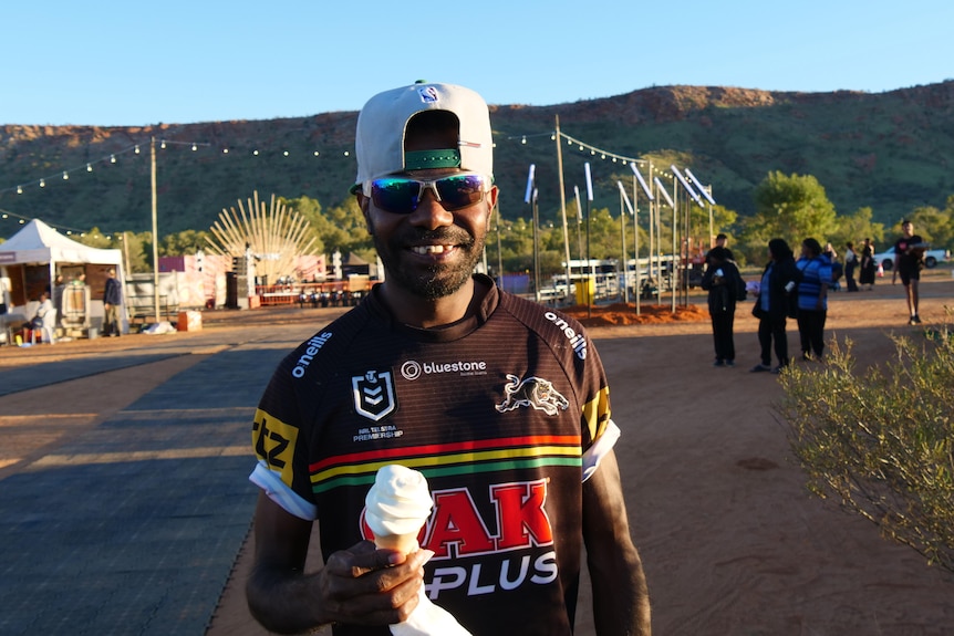 A smiling young man in a backwards cap holds an ice cream at Parrtjima festival.