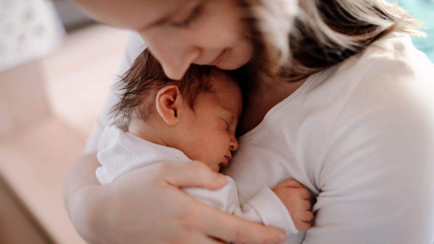 A close-up of a woman holding a newborn baby against her chest.