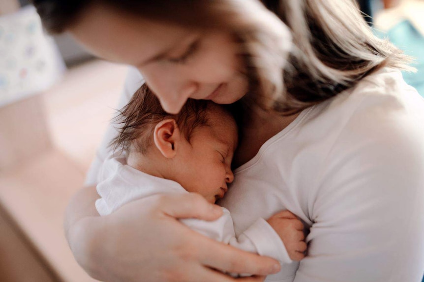 A close-up of a woman holding a newborn baby against her chest.