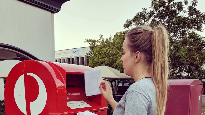 Woman standing in front of an Australia Post, holding letters ready to mail