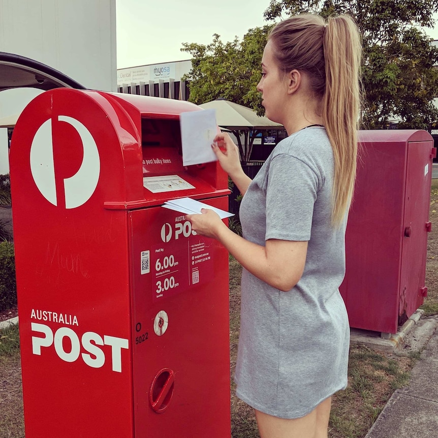 Woman standing in front of an Australia Post, holding letters ready to mail