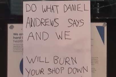 A note on a window says "do what Daniel Andrews says and we will burn your shop down"