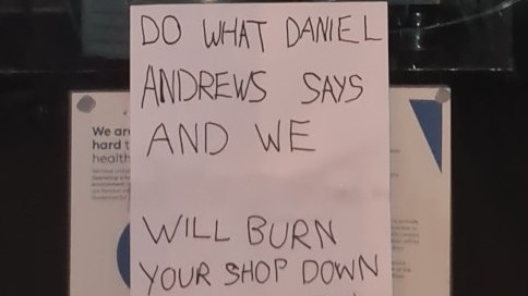 A note on a window says "do what Daniel Andrews says and we will burn your shop down"