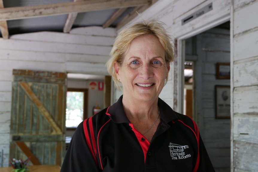 A middle-aged woman stands in a wooden cottage and smiles for a photo