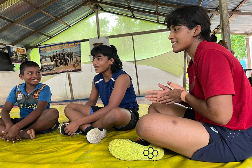 Three young Sri Lankan wrestlers sit on the mat and talk to each other.