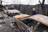 Members of a Disaster Victim Identification Team work on the remains of burnt out cars and a house.