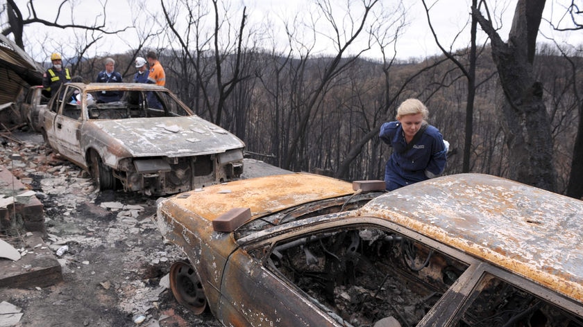 Members of a Disaster Victim Identification Team work on the remains of burnt out cars and a house.