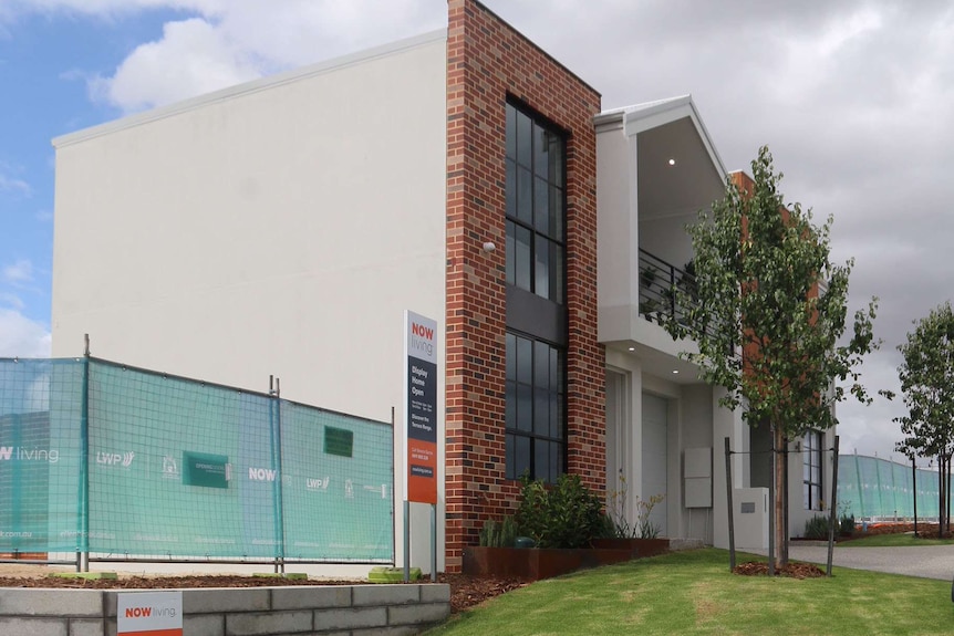 Side view of a new, two-storey micro lot display home in a housing estate with landscaping.