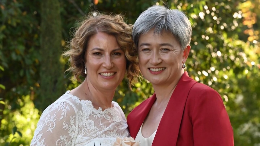 Sophie Allouache in a white dress and Penny Wong in a red blazer stand together smiling.
