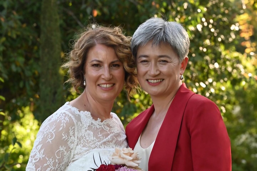 Sophie Allouache in a white dress and Penny Wong in a red blazer stand together smiling.