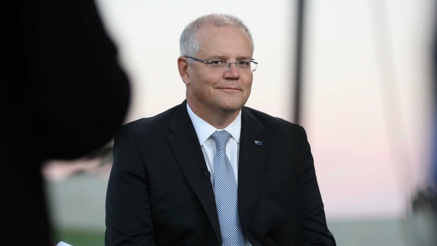 Wearing a suit and sitting on a seat, Scott Morrison smiles.