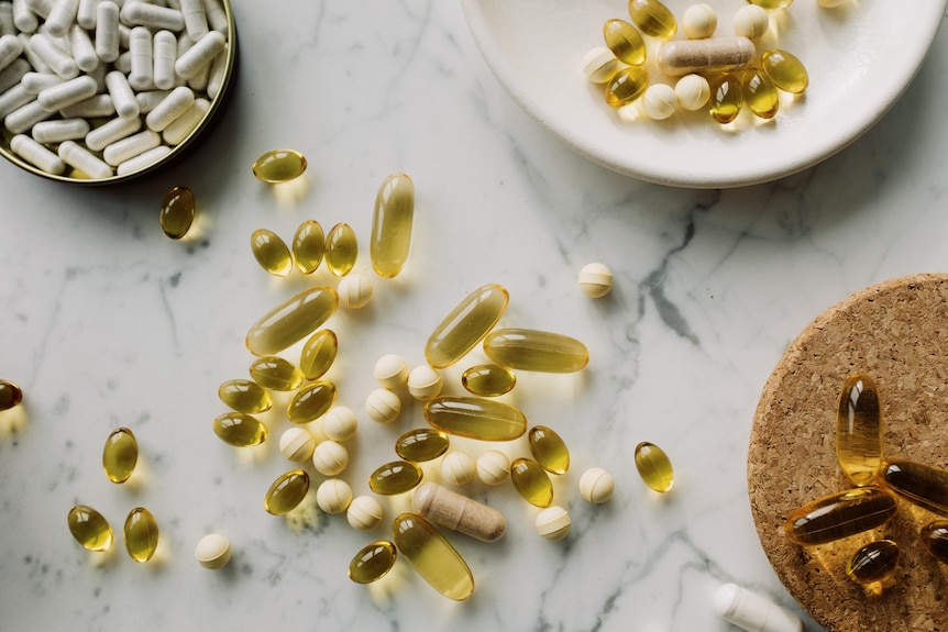Vitamins and capsules spread out on a marble benchtop, some on plates.
