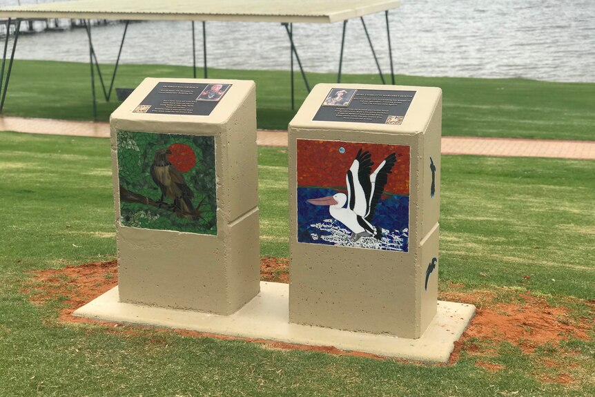 Two pillars stand on green grass, both with mosaic artworks