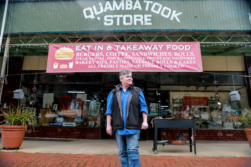 Woman in blue shirt and vest stands in front of country general store