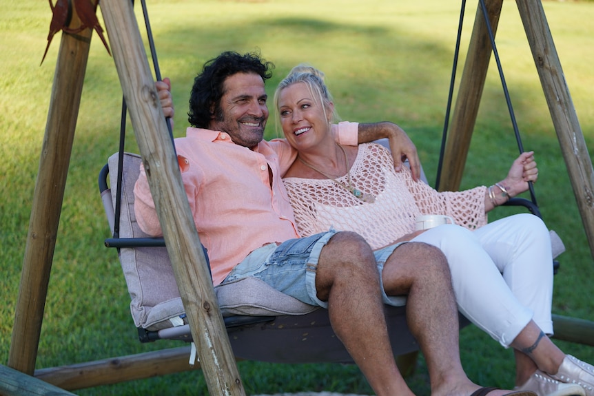 a woman smiles looking at a man as they both sit on an outdoor patio swing