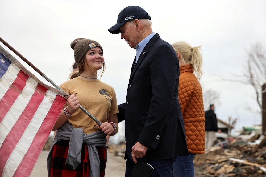 Joe Biden speaks to a girl holding a US flag. 