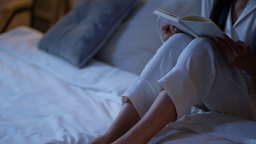 A woman sits in bed with a journal on her lap.