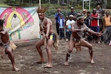 Performers in traditional dress crouch in a fighting pose as a crowd watches on.