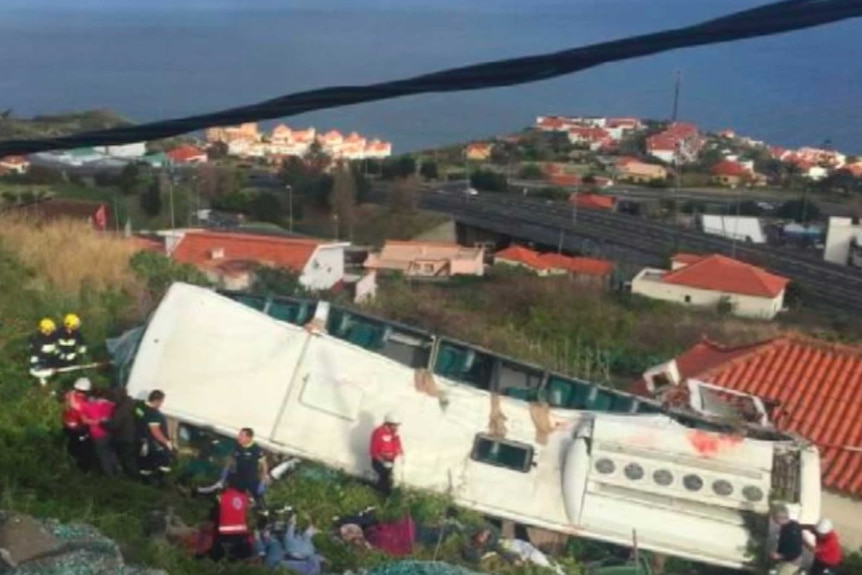 Emergency workers stand near a white bus which lies on its side at Canico.