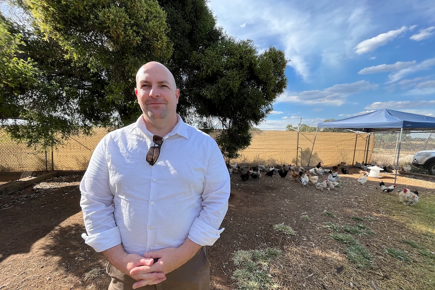 Matthew Carlin stands in the yard with chickens in the background