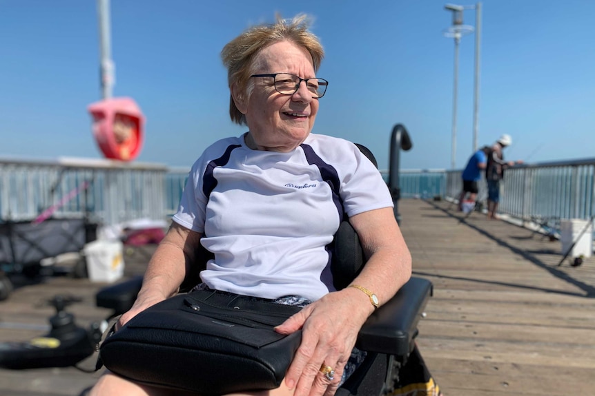 Robin Burridge in a wheelchair on a sidewalk.  She is smiling at sea.