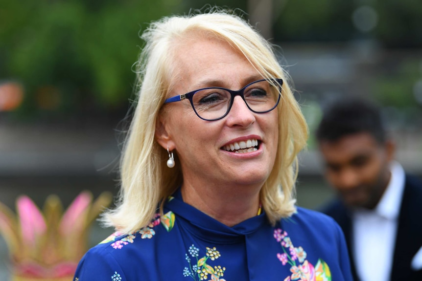 A woman with glasses and blonde hair smiles while talking