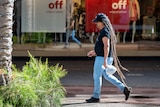 a man with dreadlocks walks down a shopping strip