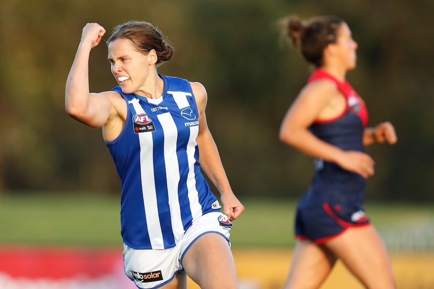 A North Melbourne AFLW player punches the air in celebration as she runs down the ground after a goal.
