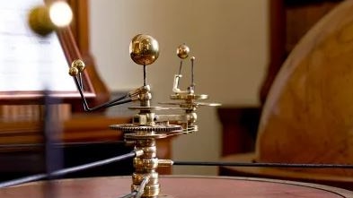 gold metal trophy-like table top structure with a sphere on a stick in centre and small spheres attached 