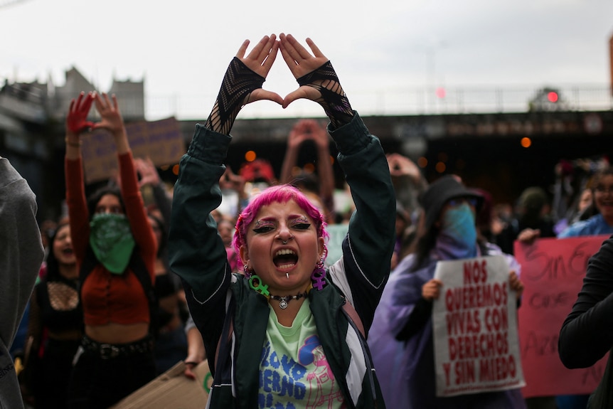 A woman holds her arms up and shouts at a women's protest. 