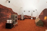 A room with red sand on the floor, on the left and right side is machinery. On the walls are printed red rocks.