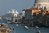 A cruise ship in the background is nearly as large as a large dome in Venice, while gondolas and vaporetto pass through a canal.