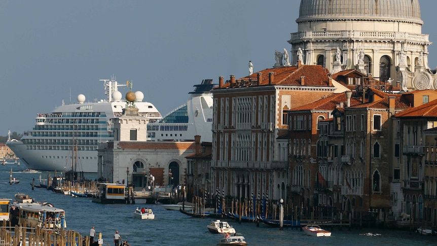 A cruise ship in the background is nearly as large as a large dome in Venice, while gondolas and vaporetto pass through a canal.