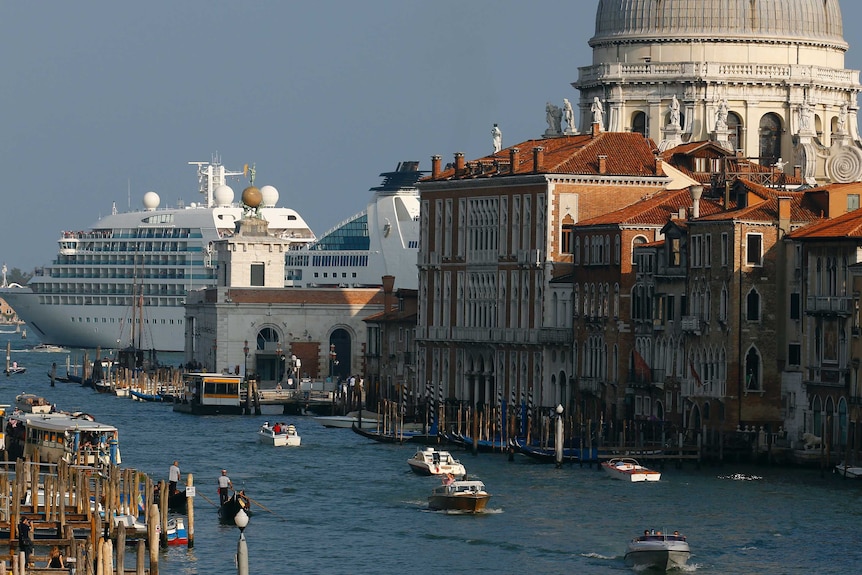 A cruise ship in the background is nearly as large as a large dome in Venice, while gondolas and vaporetto pass through a canal.