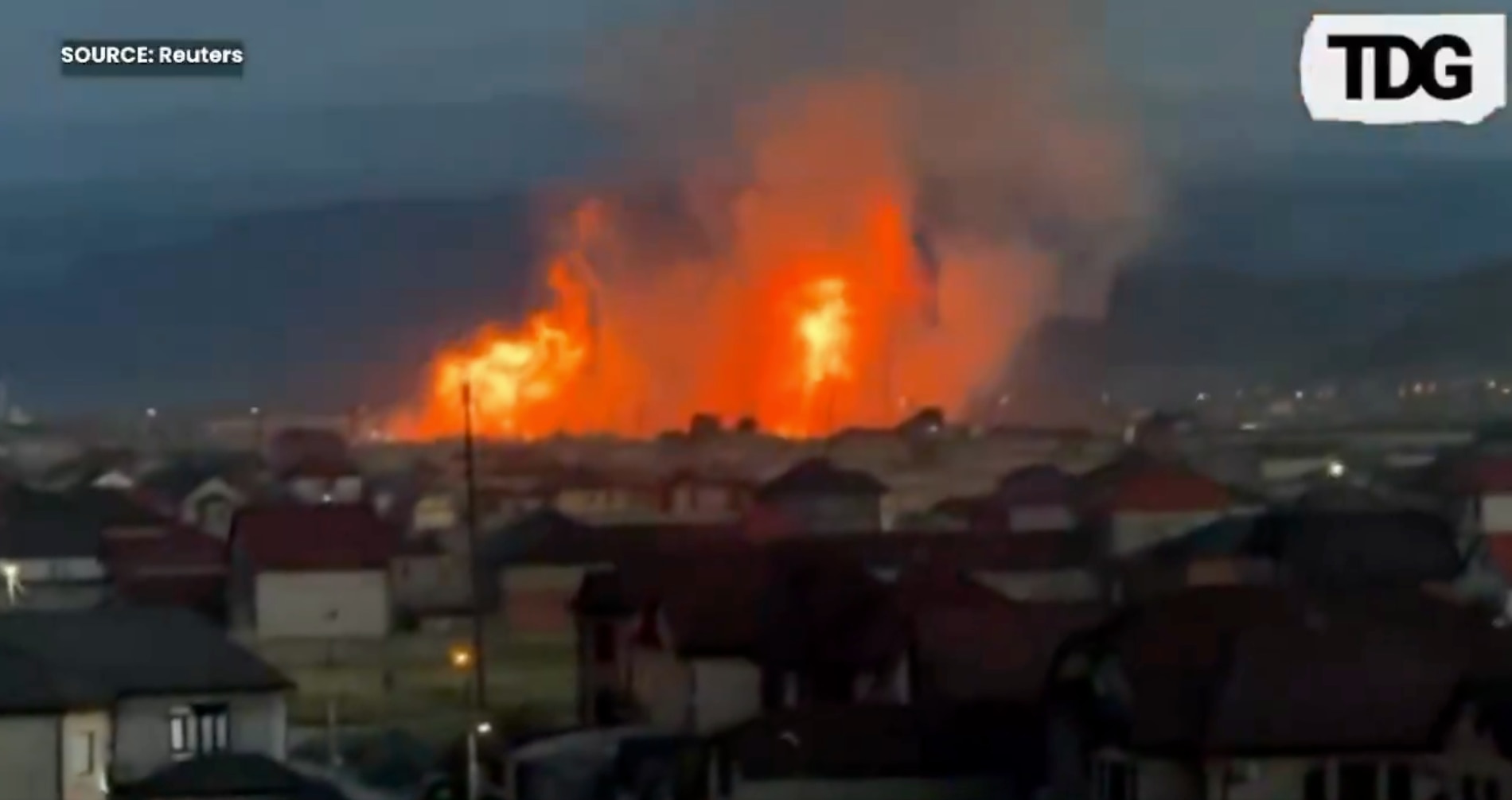 In the foreground, houses, in the background, a large set of flames.