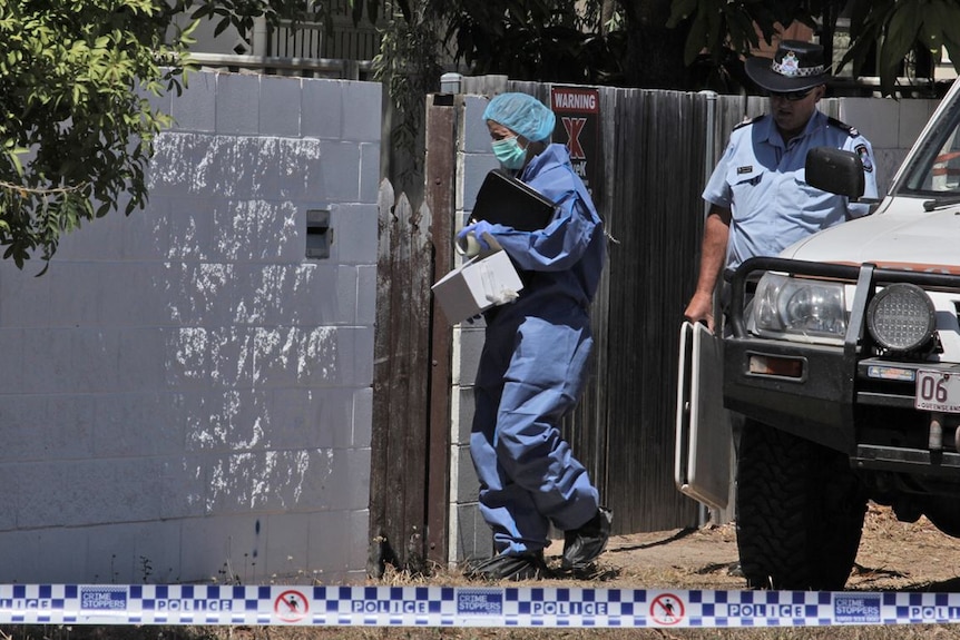 A police officer and forensic investigator walk through a gate of the house where a body was found.