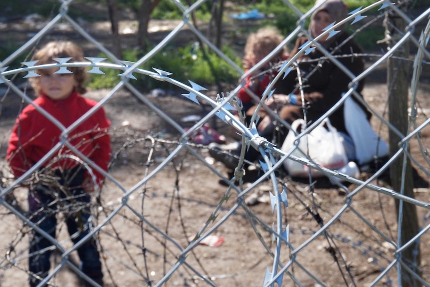 A Syrian child, out of focus, stands next to razor wire.