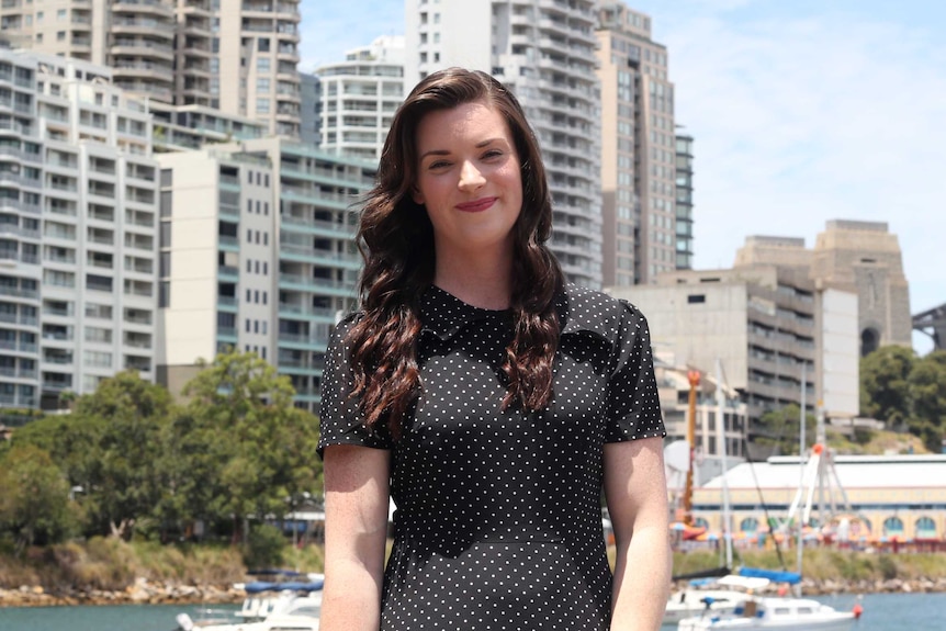 Katie Macqueen stands in front of buildings and the Sydney Harbour Bridge