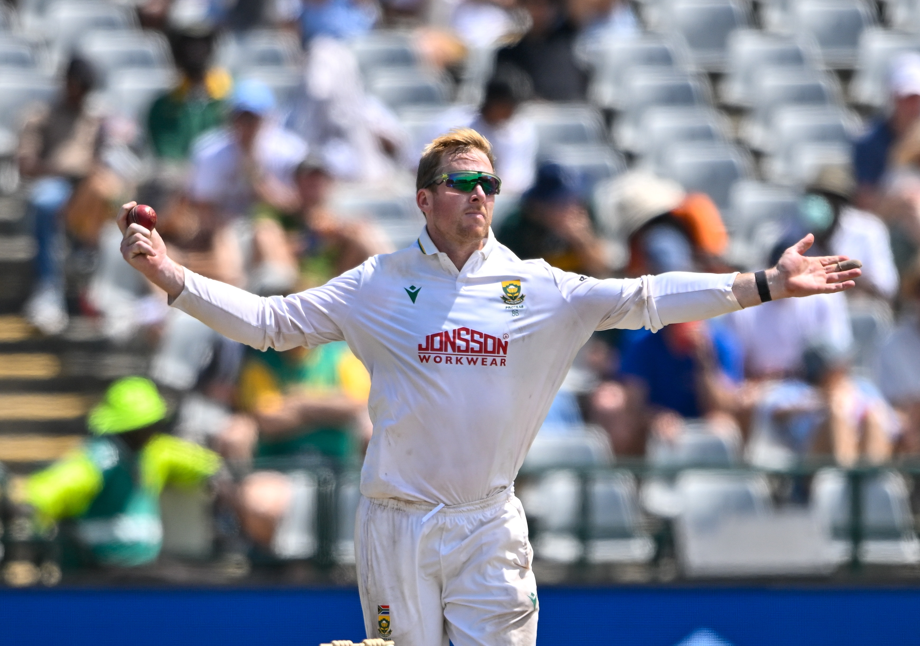 A cricketer holds his arms out with ball in hand