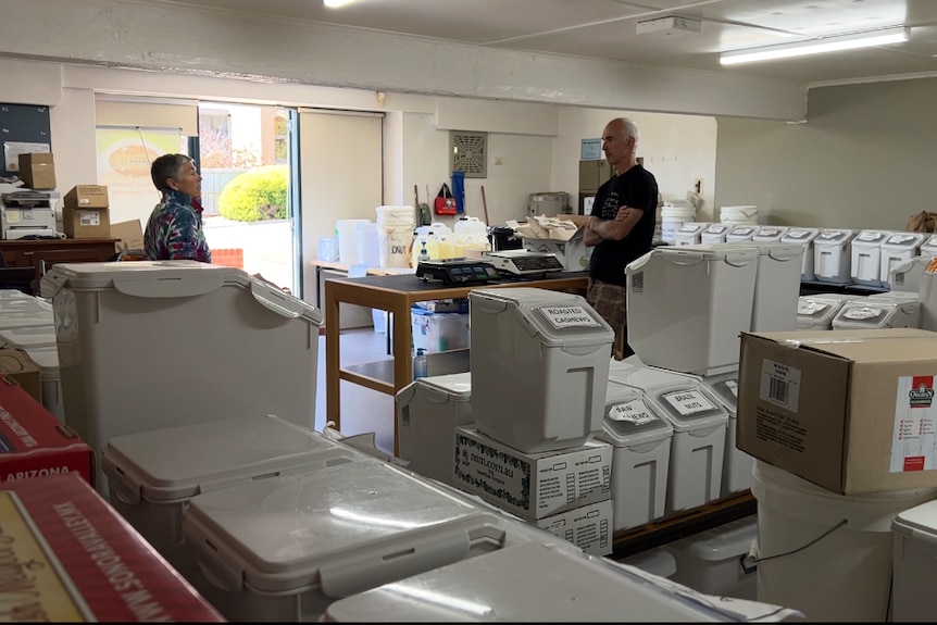 A large room full of bulk groceries in white plastic tubs. Two people stand and chat.