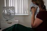 Woman with towel on face sits in front of fan