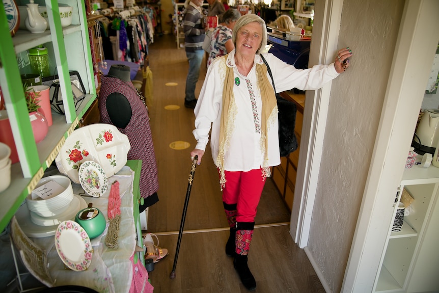 A woman smiles in the doorway of an op shop. 