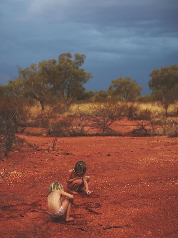 Two children play in red dirt, as a storm brews in the background.