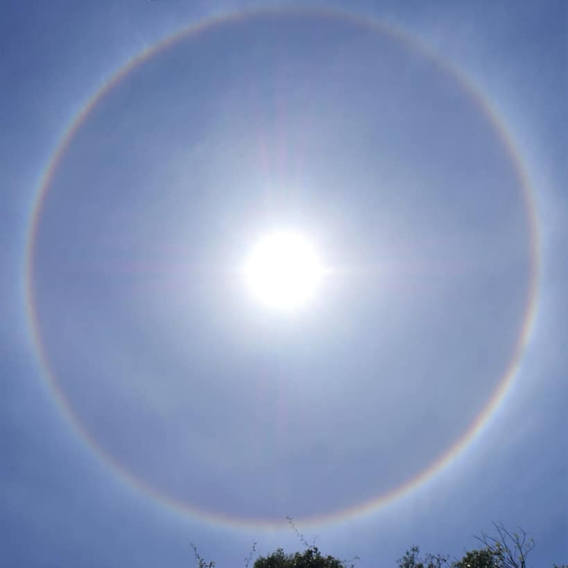 A ring of light around the sun, which beams down from a clear sky.