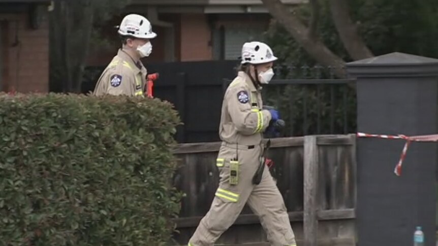 Two firefighters wearing masks walk towards a home where a fire killed one person in Bundoora.