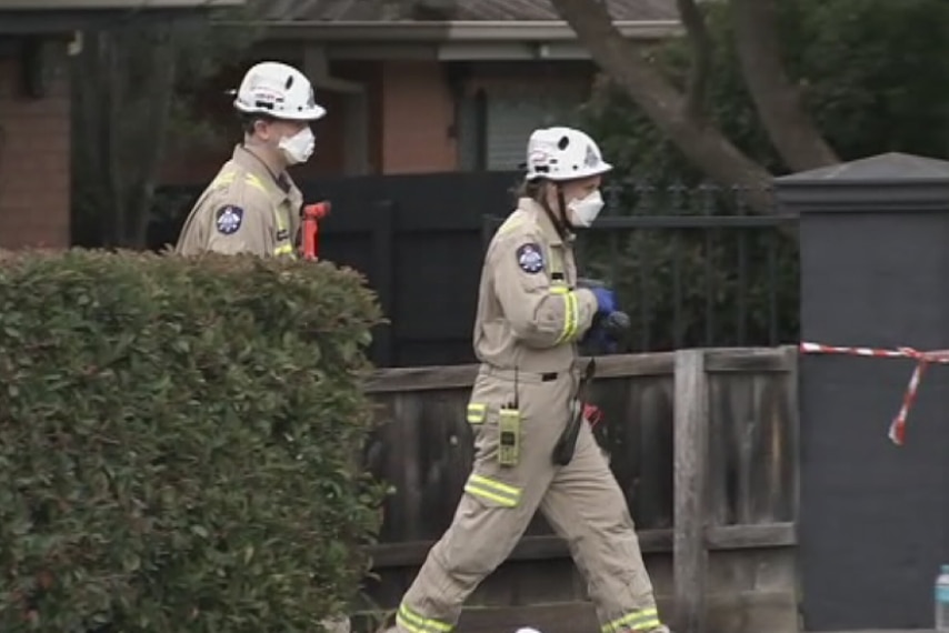 Two firefighters wearing masks walk towards a home where a fire killed one person in Bundoora.